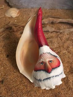 a shell with a red and white gnome face on it's side in the sand