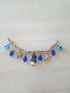 "This listing is for an UpCycled Sea Theme Charm bracelet made on a 7 1/2\" long silver tone curb chain with lobster clasp. Nine charms were wire-wrapped and added to a silver tone ring than added to the bracelet. The charms include: 2 sterling silver Starfish, 2 blue Murano Glass Square beads, 2 vintage matted blue oblong beads, 2 opaque blue glass ball beads, 2 striped, blue & white ball beads, 2 seed beads, 9 silver tone head pins. All beads are vintage along with the curb bracelet. This brac Handmade Blue Sterling Silver Charm Bracelet, Beach Charm Bracelet With Lobster Clasp, Blue Metal Charm Bracelet With Lobster Clasp, Blue Vintage Nickel Free Bracelets, Vintage Blue Nickel-free Bracelets, Blue Metal Jewelry For Beach, Vintage Blue Nickel-free Bracelet, Blue Metal Bracelets For Beach, Handmade Blue Dangle Charm Bracelet