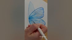 a hand is holding a blue butterfly on a white card with a pencil in it