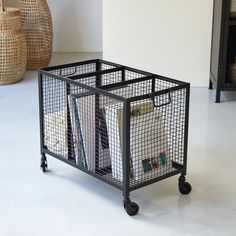 a metal cage with books and magazines in it sitting on the floor next to two vases