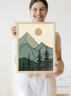 a woman is holding up a painting with mountains in the background and trees on it