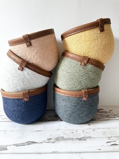 four woven baskets with leather handles are stacked on top of each other in different colors