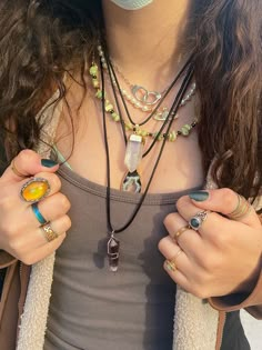 a woman wearing multiple necklaces and rings on her chest with one hand holding the other