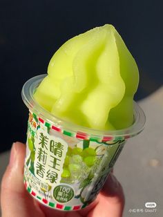 a person holding up a cup filled with ice cream covered in green jellies