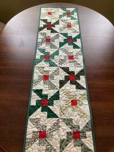 a table runner made with green, red and white quilts on top of a wooden table