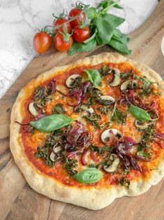 a pizza sitting on top of a wooden cutting board next to tomatoes and spinach