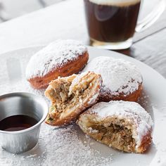 powdered sugar covered doughnuts on a plate next to a cup of coffee