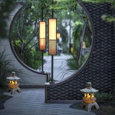 two lanterns sitting on top of a stone walkway next to a circular metal structure with trees in the background