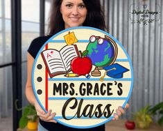 a woman holding up a sign that says mrs grace's class with an apple and book