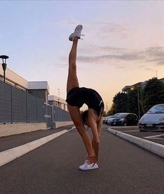 a woman doing a handstand in the middle of an empty parking lot at sunset