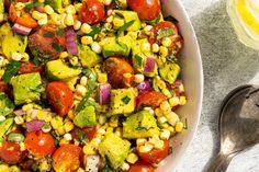 a white bowl filled with corn, tomatoes and avocado on top of a table