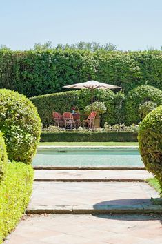 an outdoor dining area with tables and umbrellas in the distance, surrounded by hedges