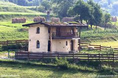 an old house in the middle of a field with hay bales on it's roof