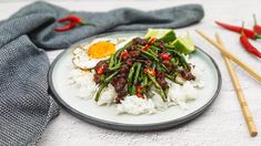 a white plate topped with rice and green beans next to chopsticks on a table