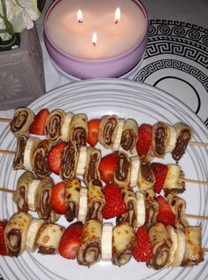 strawberries, bananas and chocolate covered pretzels on skewers next to a lit candle