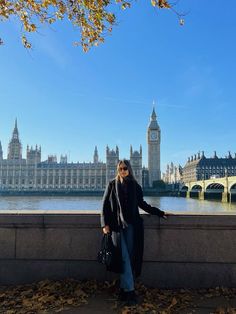 a woman leaning on a wall in front of the big ben clock tower and houses of parliament