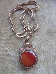 Antique agate watch fob necklace in gold fill. Our antique watch fob is adorned with a stone on each side. A carnelian colored banded agate on one side a a dark stone on the reverse make the double sided fob a striking piece. It suspends from a 16'' gold fill chain that closes with an old fashioned C thumb spring clasp. A swivel hook acts as the bail and brings the pendant to a length of one and seven eighths of an inch x .75''. The fob is older than the chain which may date to the 1930s. These pieces exhibit age appropriate wear with some scratching and finish loss. This estate found necklace will make an interesting layering necklace with your other antique pieces. Gold Carnelian Jewelry With Polished Finish, Vintage Jewelry With Polished Finish For Memorials, Antique Red Medallion Jewelry, Vintage Medallion Necklace With Polished Finish, Vintage Carnelian Jewelry With Polished Finish, Vintage Medallion Jewelry With Polished Finish, Classic Agate Jewelry With Polished Finish, Vintage Polished Carnelian Jewelry, Formal Agate Pendant Jewelry