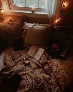 an open book on a bed next to a window with some lights in the corner