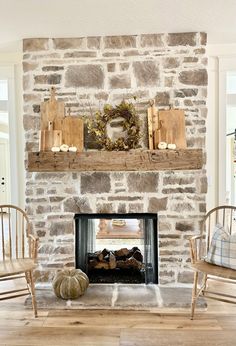 a stone fireplace with two chairs and a wreath on the mantel above it in a living room