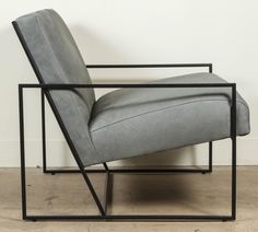 a grey leather chair sitting on top of a wooden floor next to a white wall