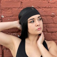 a woman with black hair wearing a headband against a red brick wall and posing for the camera