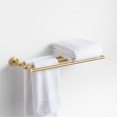 a towel rack with two white towels hanging on it's gold bar, against a white wall