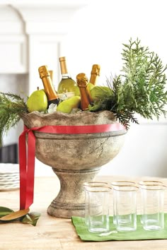 a bowl filled with wine bottles and apples on top of a table next to glasses