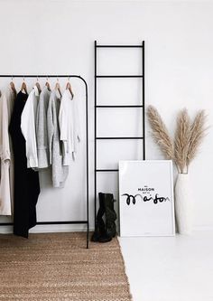 a white room with clothes hanging on the rack and a black ladder next to it