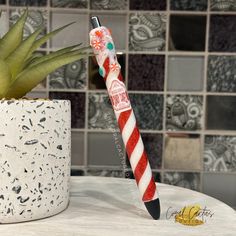 a red and white striped pen sitting on top of a table next to a potted plant