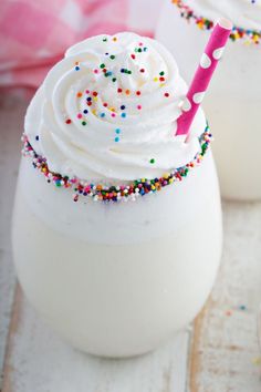 two glasses filled with white frosting and sprinkles next to spoons