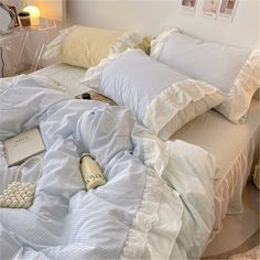 an unmade bed with blue and white sheets, pillows and a bottle of perfume