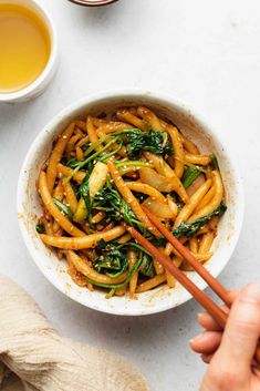 someone holding chopsticks over a bowl of stir fry noodles with spinach and carrots