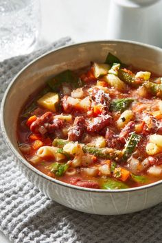 a white bowl filled with vegetable soup on top of a table next to a cup