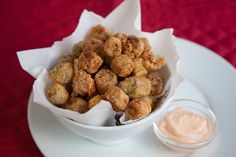 a white bowl filled with fried food on top of a plate next to dipping sauce