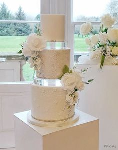 three tiered wedding cake sitting on top of a white box in front of a window