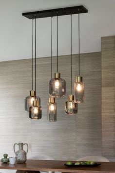 a dining room table and chairs with lights hanging from the ceiling above it in front of a wall