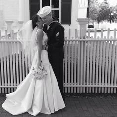 a bride and groom kissing in front of a white picket fence