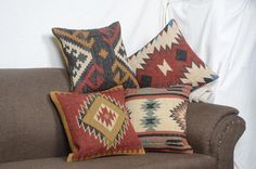 three colorful pillows are sitting on a brown couch