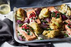 a tray filled with salmon and vegetables next to a glass of wine on a table