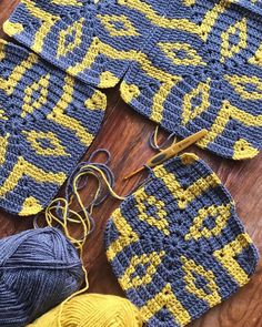 several crocheted squares and balls of yarn on a wooden table with knitting needles