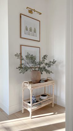 a white table topped with a potted plant next to a framed painting on the wall