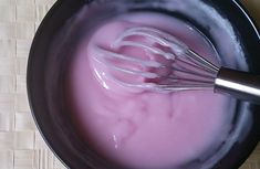 two whisks in a black bowl with pink liquid