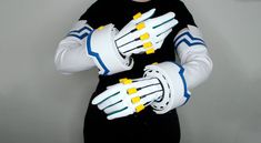 a person wearing white and blue gloves with yellow fingertipss on their hands, standing in front of a gray wall