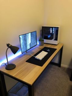 a desk with a computer monitor, keyboard and mouse next to a lamp on it