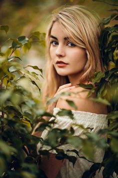 a beautiful blonde woman with blue eyes posing for a photo in the woods by some leaves