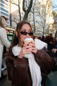 a woman drinking from a cup while wearing sunglasses