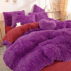 a bed covered in purple fluffy pillows next to a red comforter and pillow case