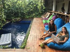 two women sitting on bean bag chairs with laptops in front of a swimming pool