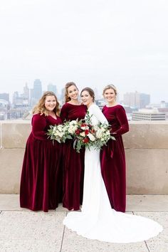 four bridesmaids in velvet dresses pose for a photo on top of a building