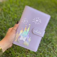 a hand holding a purple passport case with disney castle on it